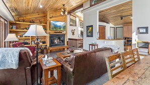 Ein gemütliches Wohnzimmer mit Kamin, Ledersofa, Holzboden und einem Essbereich mit Holztisch und Stühlen.