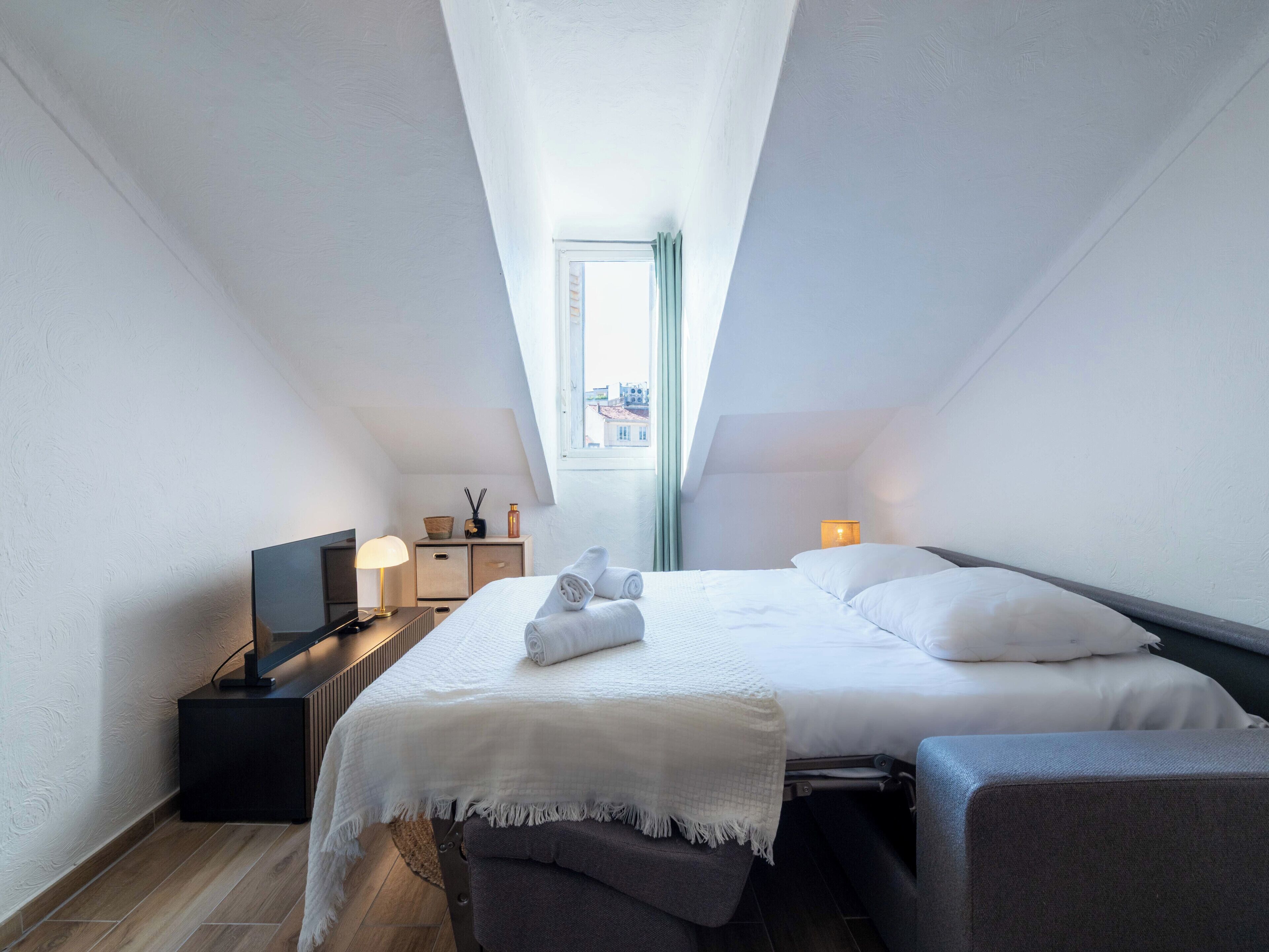 A modern, well-lit room with a bed, bedside table, lamp, and a view through a skylight.