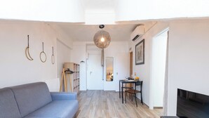 A modern living room with a grey sofa, wooden flooring, a hanging light fixture, and a TV on a wooden stand. - Top Floor Studio – Heart of Cannes (Cannes)