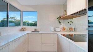 Eine moderne Küche mit weißen Schränken, einem großen Fenster und Blick auf Grünfläche.