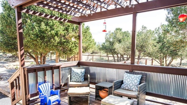 A covered outdoor seating area with cushioned chairs and a table, surrounded by wooden railings and trees. - Princeton View 3BR w/perfect backyard for dogs (Buena Vista)
