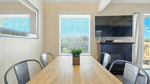 Uma sala de jantar com mesa de madeira, cadeiras, um vaso de planta, televisão e lareira.
