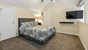 Quarto com cama, ventilador de teto, televisão e porta.