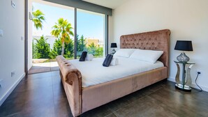 Un dormitorio con una cama grande, dos lámparas de noche, vista a palmeras y una puerta corrediza de vidrio.