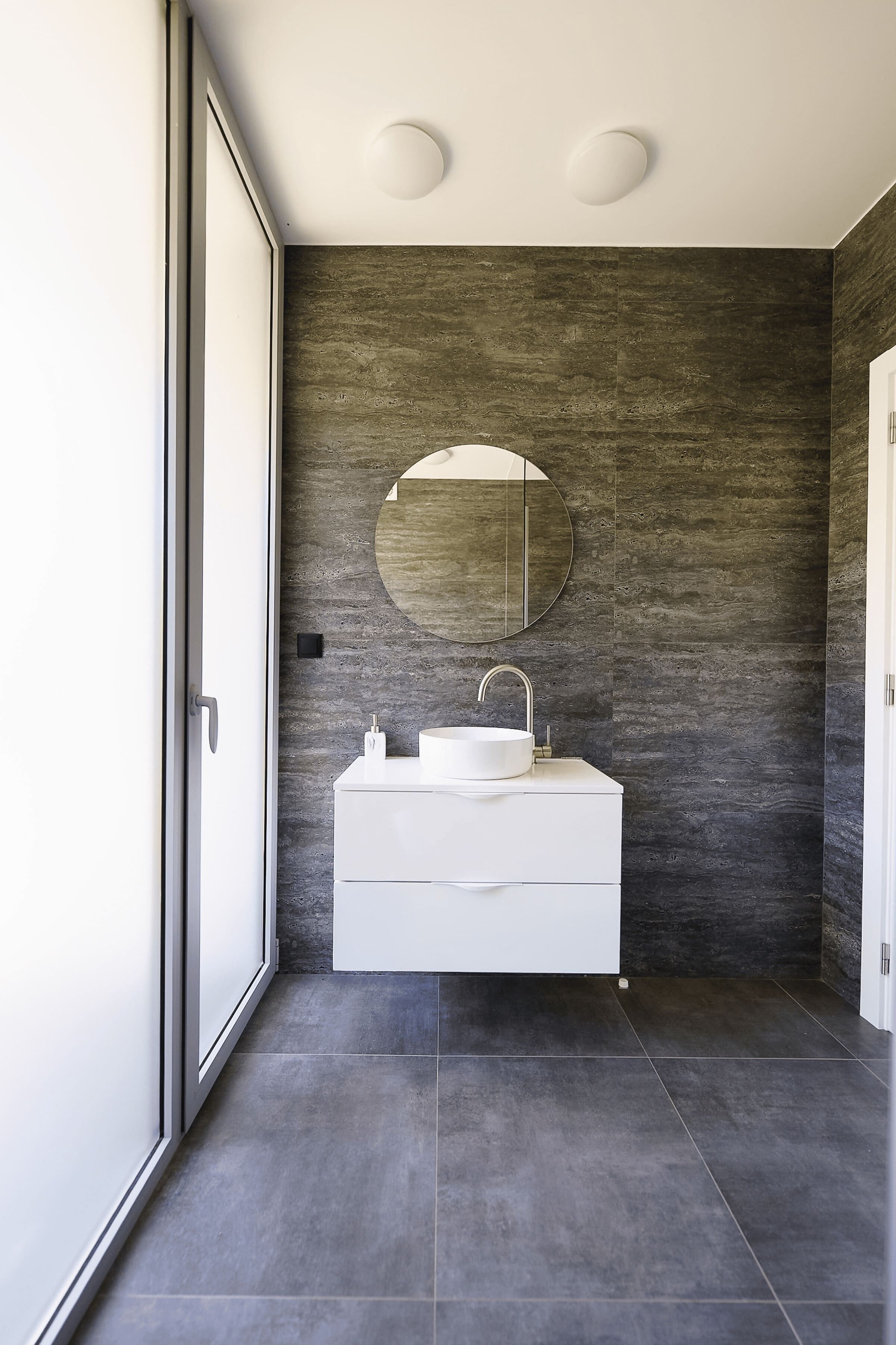 Une salle de bain moderne avec un grand miroir, un meuble-lavabo blanc et des murs à texture foncée.