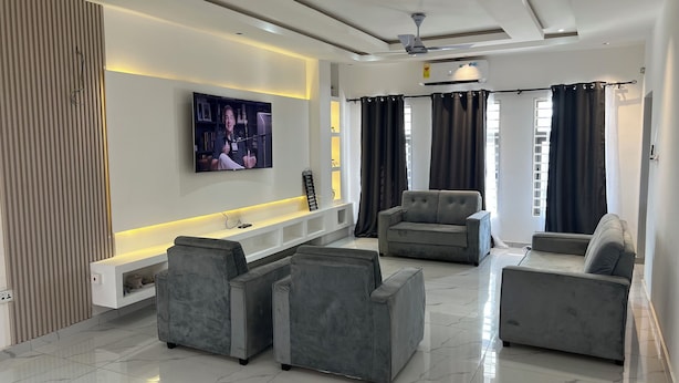 A modern living room with a flat-screen TV, grey sofas, a coffee table, and a ceiling fan. - 1BR Ultra Modern House in Gbawe (Accra)