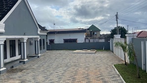 A paved courtyard with a white building featuring a black roof and a green-roofed structure in the background. - 1BR Ultra Modern House in Gbawe (Accra)