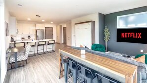 A modern kitchen with white cabinets, a wooden countertop, and a bar area with stools. - Modern 5th Floor Sky Suite Retreat - 1BR Sleeps 6 (Milwaukee)