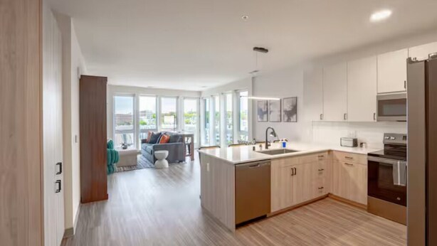 A modern kitchen with a central island, stainless steel appliances, and a view to the living area. - Modern 5th Floor Sky Suite Retreat - 1BR Sleeps 6 (Milwaukee)