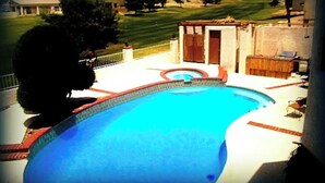 Uma piscina com borda azulejada, um deck de madeira e um pequeno galpão ao fundo.