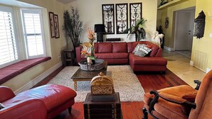 Uma sala de estar com um sofá vermelho, uma poltrona marrom e uma mesa de centro com objetos decorativos.