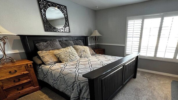 Quarto com cama, mesas de cabeceira de madeira, espelho e janela com persianas.