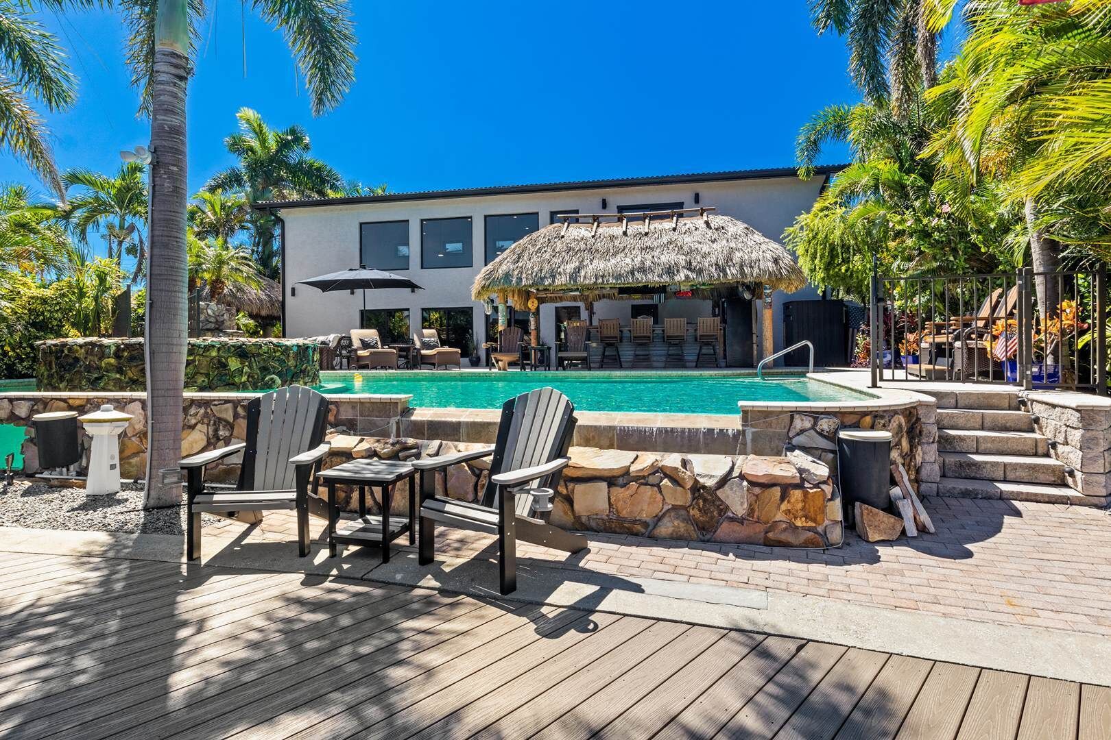 A pool area with lounge chairs, a thatched-roof structure, and a stone wall.