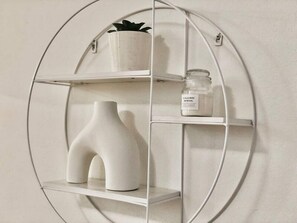 A white, circular, wall-mounted shelf unit with three shelves, each holding a white vase, a small potted plant, and a glass jar with a label. - 83 OSHR (Bondi Junction)