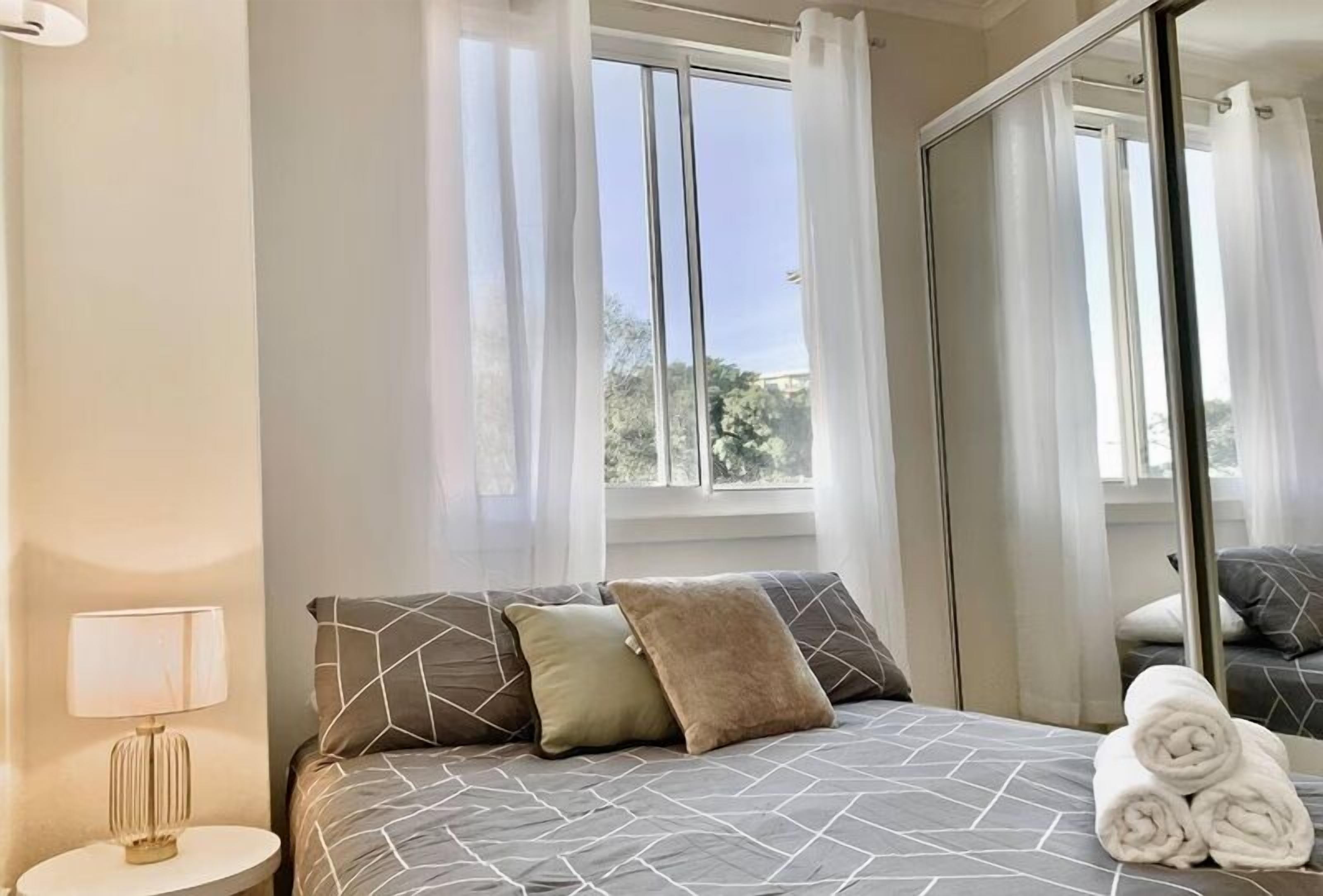 A bedroom with a bed, a nightstand, a lamp, and a window with curtains.