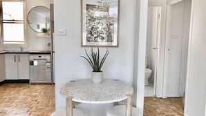 A modern kitchen with white cabinets, a dishwasher, and a round table with a potted plant. - 83 OSHR (Bondi Junction)