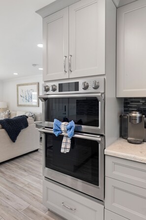 A modern kitchen with stainless steel appliances, white cabinetry, and a blue towel on the oven handle. - Open Water Views, NEW Pool, Elevator & Easy Boating from Modern Canal Home (Cudjoe Key)
