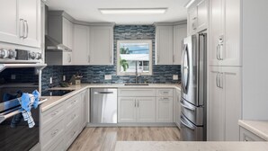 A modern kitchen with white cabinets, stainless steel appliances, a tiled backsplash, and a window with a view. - Open Water Views, NEW Pool, Elevator & Easy Boating from Modern Canal Home (Cudjoe Key)