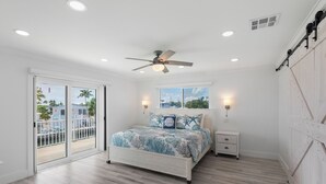 A bedroom with a bed, a ceiling fan, a nightstand, and a sliding glass door leading to a balcony. - Open Water Views, NEW Pool, Elevator & Easy Boating from Modern Canal Home (Cudjoe Key)
