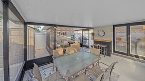 A covered patio with a glass table and chairs, a sofa, and a clock on the wall.