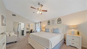 A bedroom with a large bed, a nightstand, a ceiling fan, and a mirror.