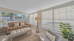 Un salon avec un canapé beige, un pouf assorti et une lampe sur pied.