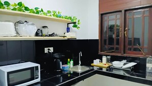 A compact kitchen with a microwave, kettle, and coffee maker on the counter, a sink, and a window with wooden shutters. - Yala Quest Safaris/Tours/HomeStay - Tissamaharama (Mahasenpura, Tissamaharama)
