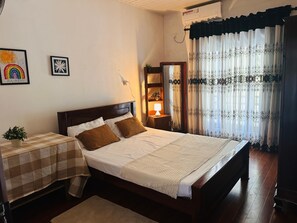 Een slaapkamer met een bed, nachtkastje, lamp en gordijnen.