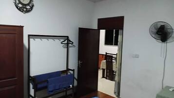 A room with a bed, a wardrobe, a mirror, a fan, and a door leading to another room.