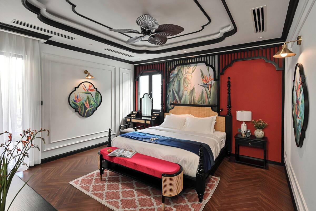 Un dormitorio con cama, banco, mesita de noche y una obra de arte.