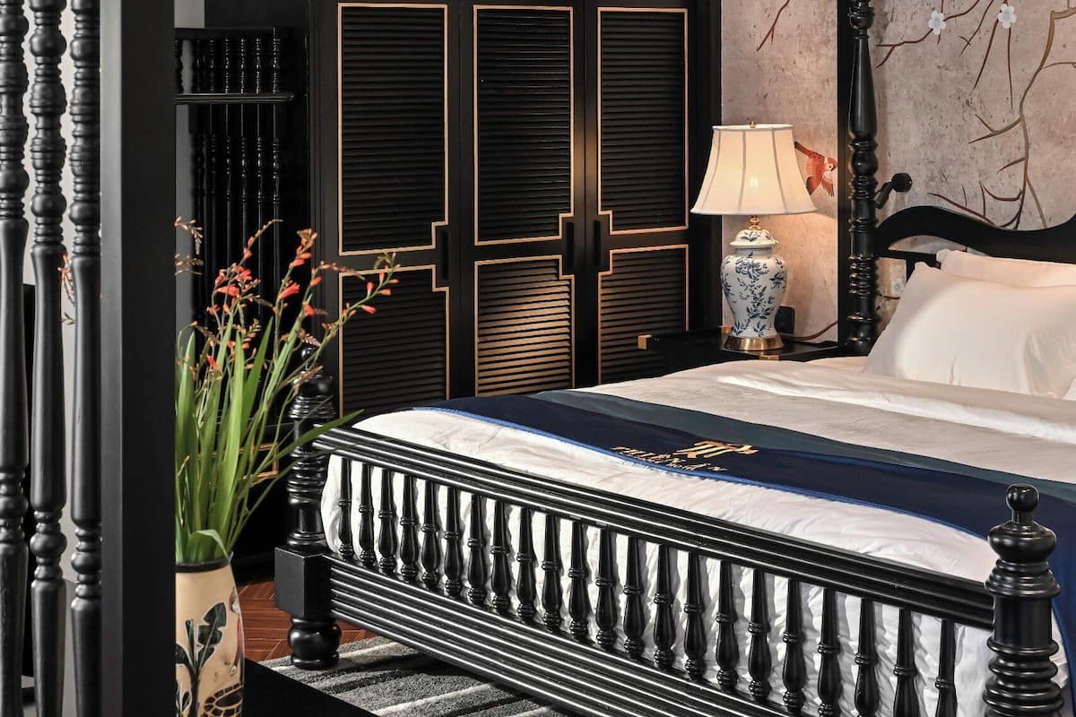 Un dormitorio con cama, mesita de noche, lámpara y planta en maceta.