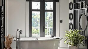 A bathroom with a freestanding bathtub, a large window, and a potted plant.