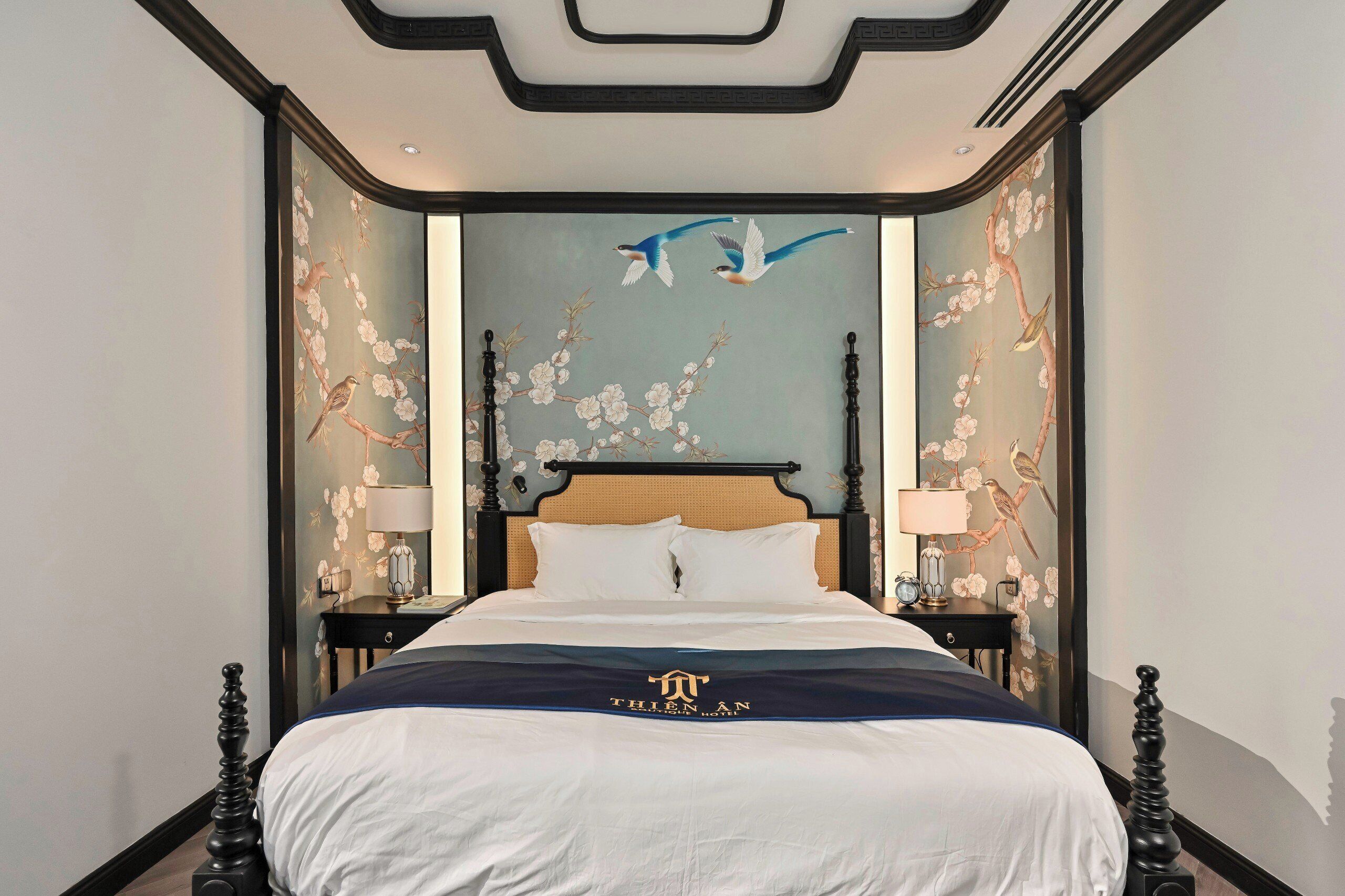 Una habitación de hotel con una cama grande, una mesita de noche con lámpara y una pared con un mural de flores y pájaros.