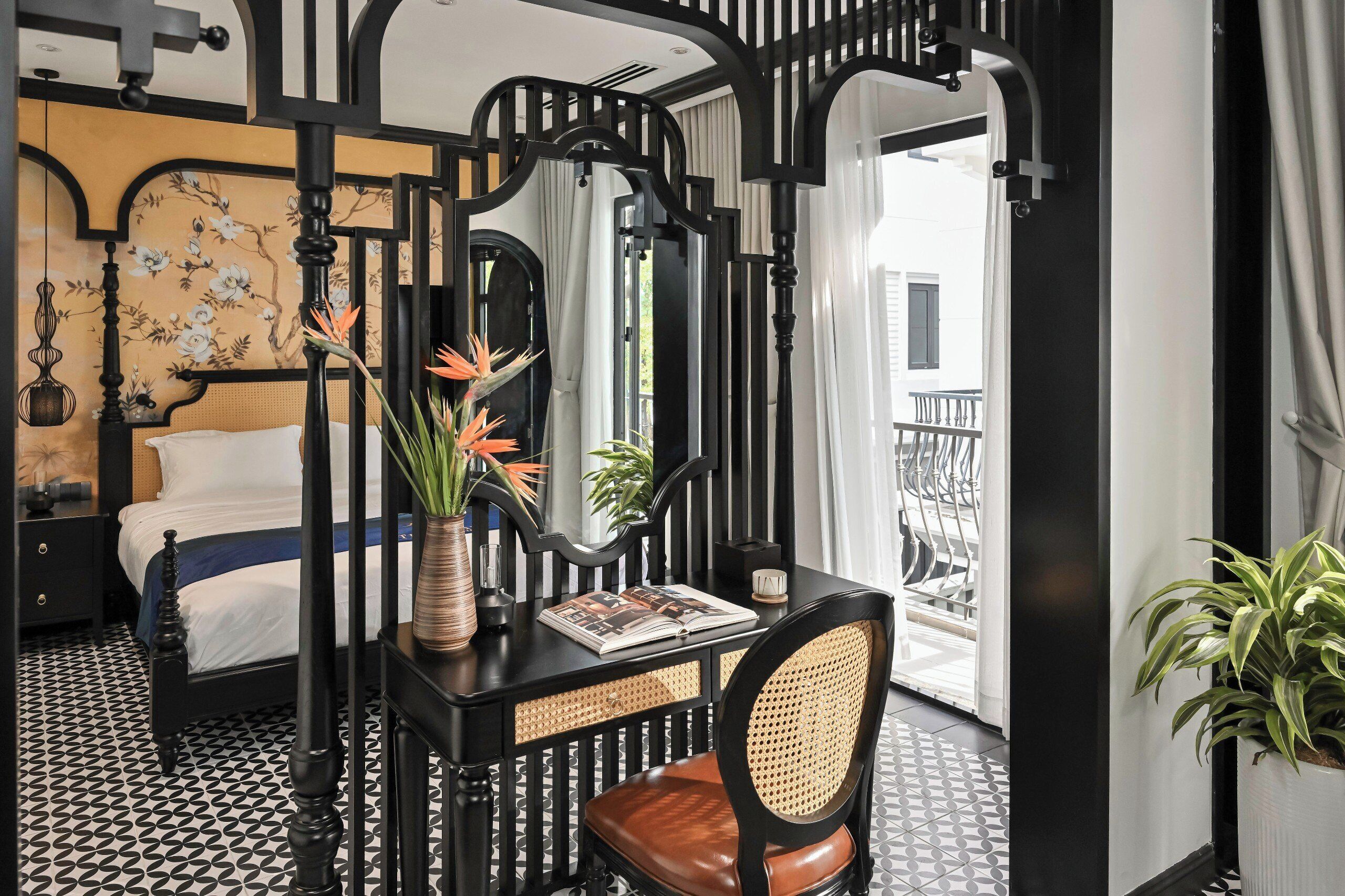 A bedroom with a bed, a desk with a chair, a mirror, and a potted plant.