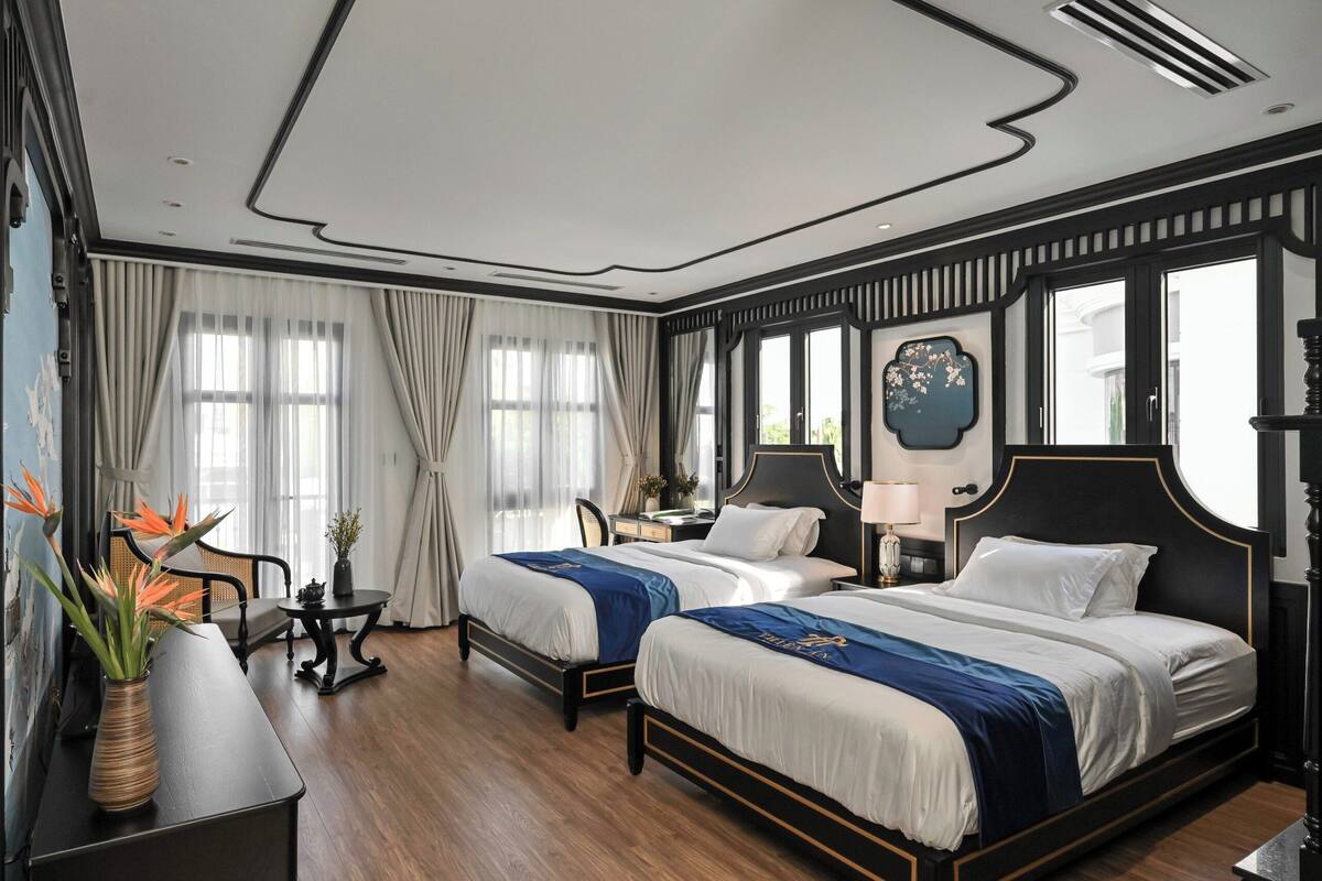 Habitación de hotel con dos camas, un escritorio, una silla y un ventanal con cortinas.