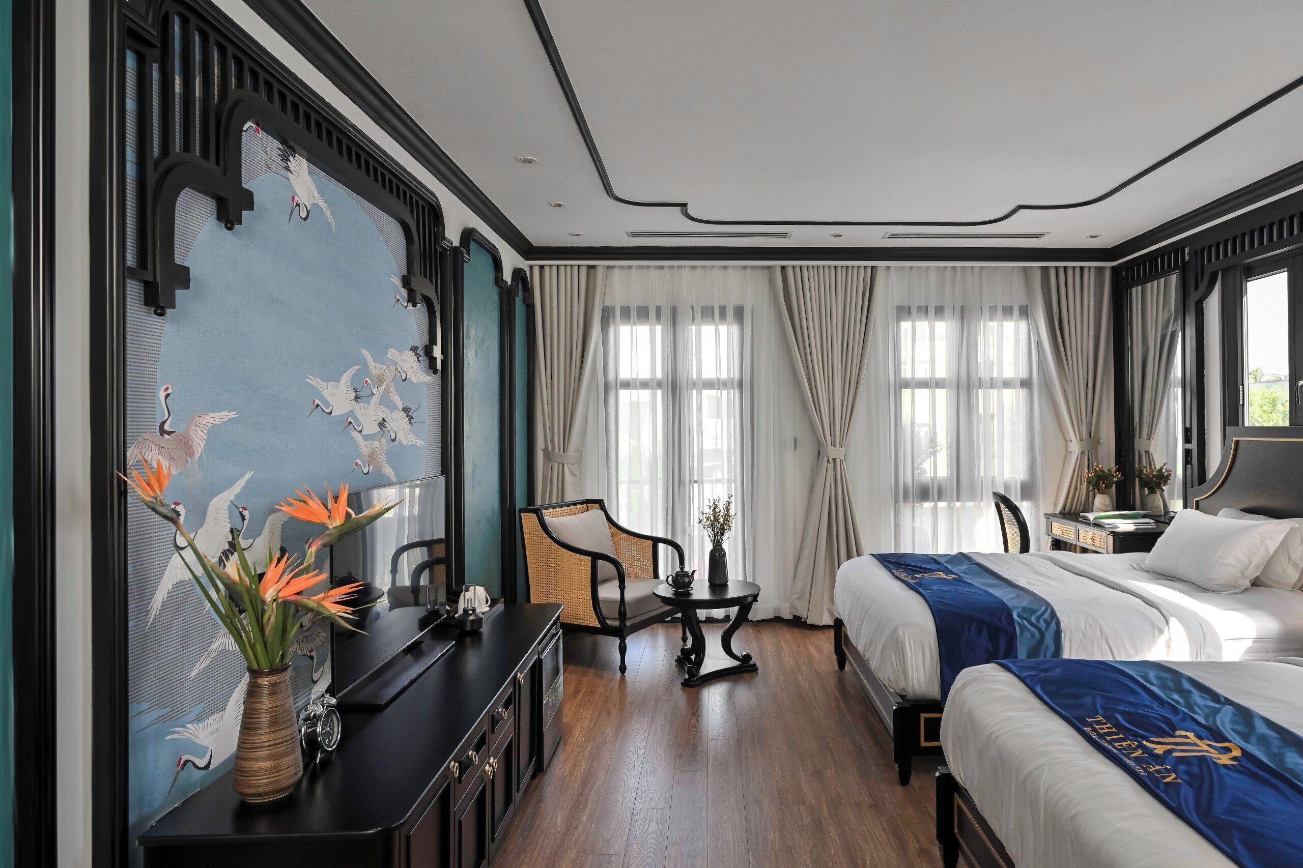 Une chambre d’hôtel avec deux lits, un bureau, une chaise, un vase avec des fleurs et un mur orné d’une fresque.