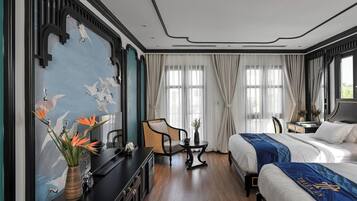 Une chambre d’hôtel avec deux lits, un bureau, une chaise, un vase avec des fleurs et un mur orné d’une fresque.