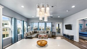 A modern living room with a large central island, a sectional sofa, and a television on the wall. - Steps to the Beach l Modern Interior (Crystal Beach)
