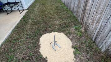 Um quintal com cerca de madeira, um pátio de concreto e um objeto de metal na grama.