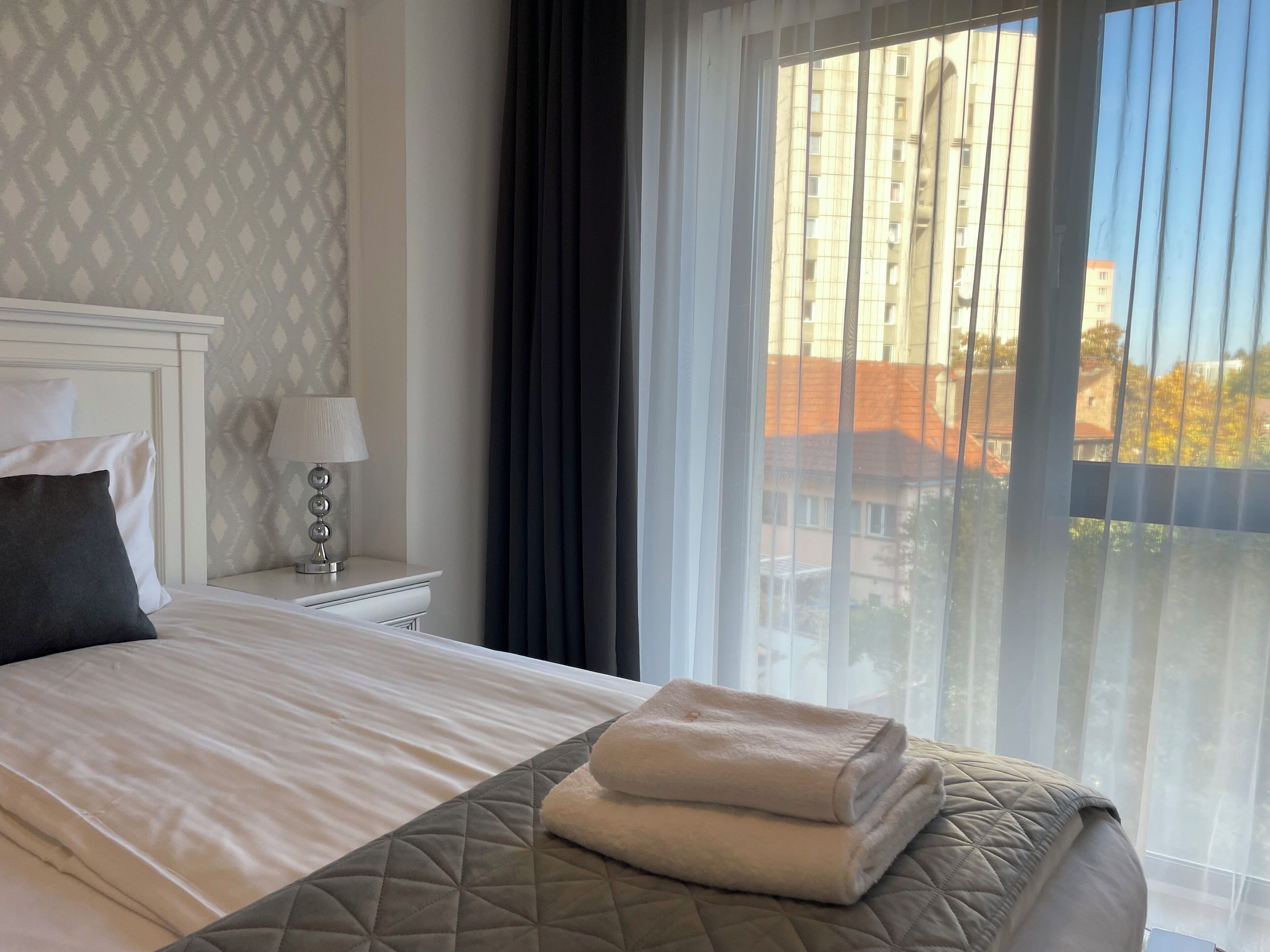 A neatly made bed with a quilted headboard, a bedside lamp, and a window with sheer curtains.
