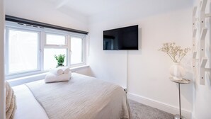 Une chambre moderne avec un grand lit, un téléviseur à écran plat fixé au mur et une fenêtre donnant sur l’extérieur.