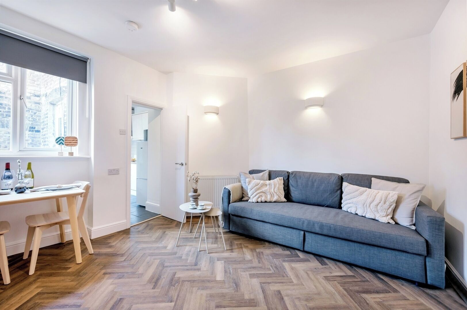 A modern living room with a grey sofa, wooden floor, and a white desk with chairs.