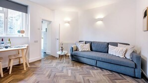 Un salon moderne avec un canapé gris, un plancher en bois et un bureau blanc avec des chaises.