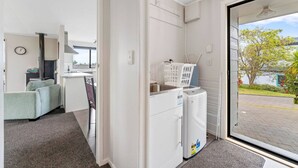 Ein kompakter Wohnraum mit Küchenzeile, einer Couch, einer Waschmaschine und Blick ins Freie.