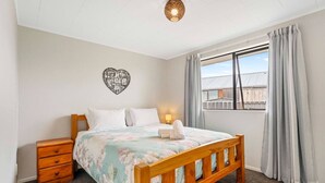 Ein Schlafzimmer mit einem hölzernen Bett, einem Nachttisch, einem Wandbild und einem Fenster mit Vorhängen.