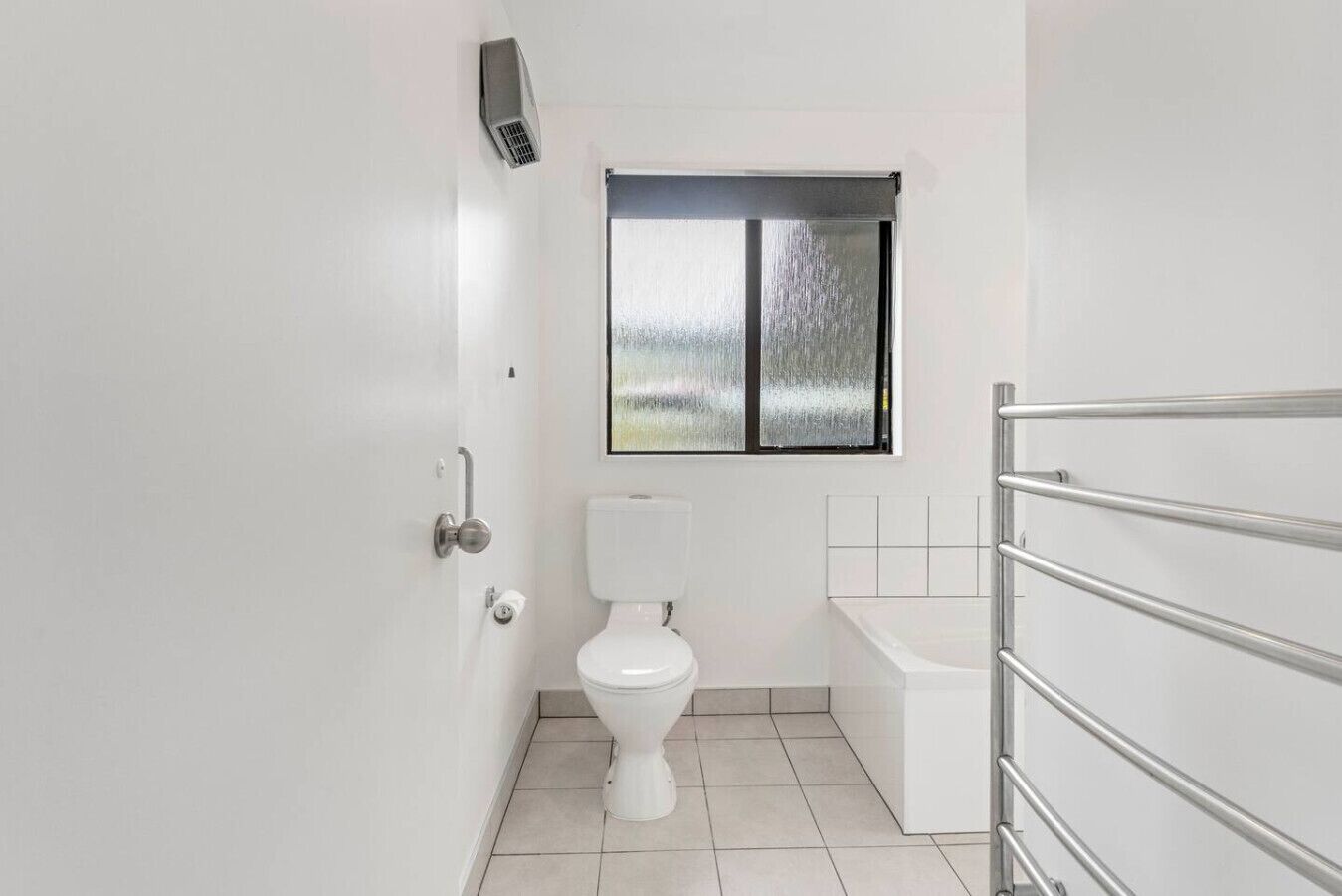 A small, modern bathroom with a toilet, a window, and a shower area.