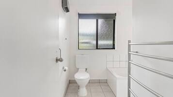 A small, modern bathroom with a toilet, a window, and a shower area.