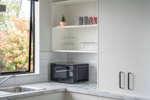 Une cuisine avec des meubles blancs, un four à micro-ondes et des étagères où sont disposés de la verrerie et des objets décoratifs.