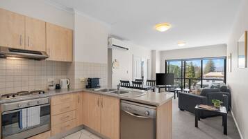 A modern kitchen with a dishwasher, stove, and a dining area with a TV and seating.