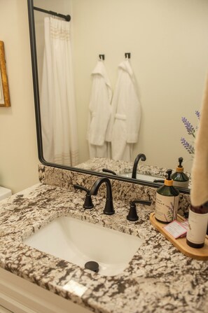 A bathroom with a granite countertop, a sink, a mirror, and two white towels hanging on hooks. - Modern 3-bedroom house near downtown Forest City with a private backyard. (Forest City)